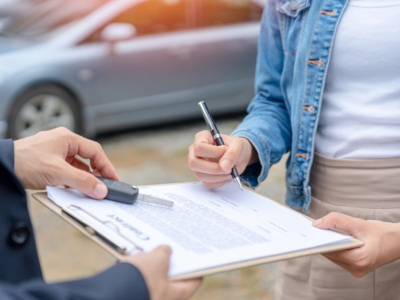 Customer signing a rental contract and receiving car keys – how do you rent a car.