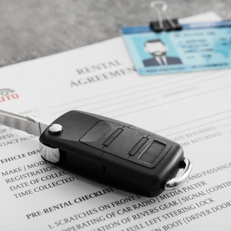 A car key placed on a rental agreement with an ID card nearby, representing the steps to compare rental car deals.